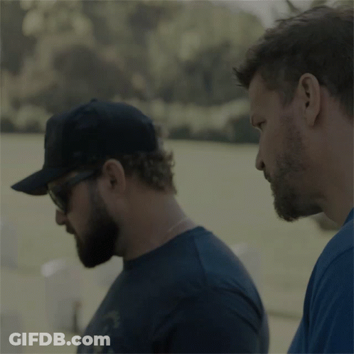 A Man Wearing A Black Hat And Sunglasses Holds Another Man 'S Shoulder GIF