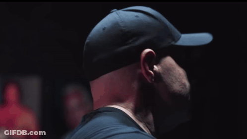 A Man Wearing A Black Hat And Sunglasses Looks To His Left GIF