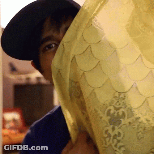 A Man Wearing A Black Hat Is Peeking Out From Behind A Yellow Curtain GIF