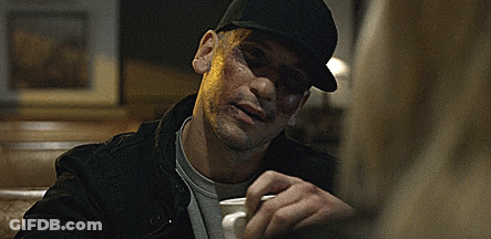 A Man Wearing A Black Hat Is Sitting At A Table Holding A Cup Of Coffee GIF