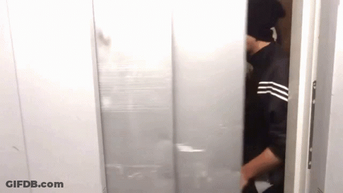 A Man Wearing A Black Hat Is Standing In A Doorway . GIF