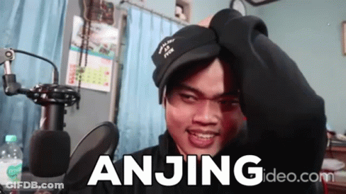 A Man Wearing A Black Hat Is Standing In Front Of A Microphone And The Word Anjing Is On The Screen Behind Him GIF