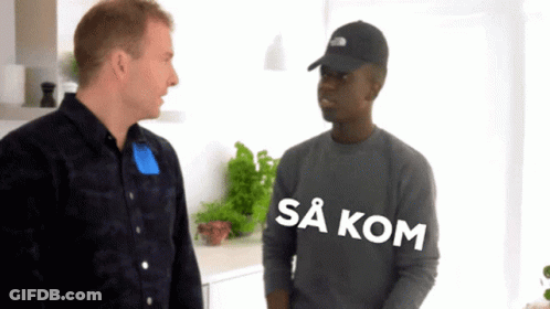 A Man Wearing A Black Hat Talks To Another Man Who Is Wearing A Grey Shirt That Says Sa Kom GIF