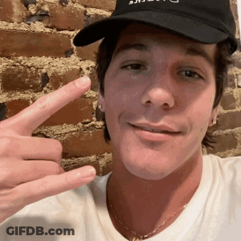 A Man Wearing A Black Hat That Says ' U.s.a. ' On It Is Making A Peace Sign GIF