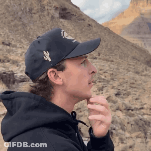 A Man Wearing A Black Hat With A Cactus On It Looks To The Side GIF