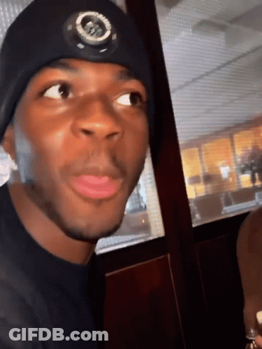 A Man Wearing A Black Hat With A Circle On It Looks At The Camera GIF
