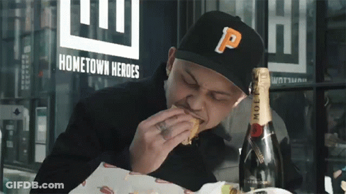 A Man Wearing A Black Hat With The Letter P On It Is Eating A Sandwich GIF