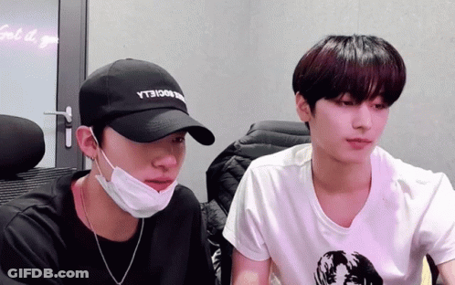 A Man Wearing A Black Hat With The Word Yt3 On It Sits Next To Another Man Wearing A Mask GIF