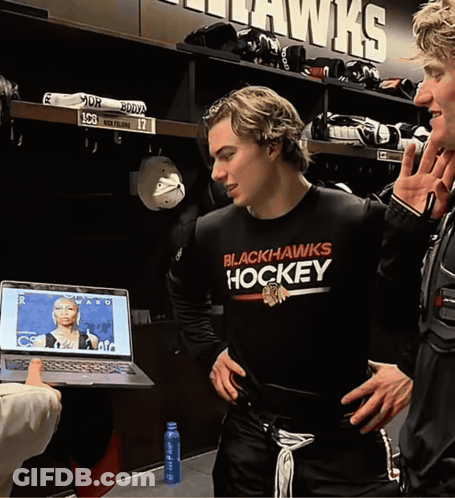 A Man Wearing A Black Hawks Hockey Shirt Stands In A Locker Room GIF