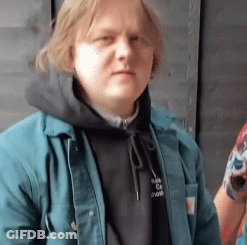 A Man Wearing A Black Hoodie And A Blue Jacket Looks At The Camera . GIF