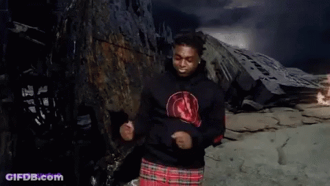 A Man Wearing A Black Hoodie And A Plaid Skirt Is Dancing In Front Of A Mountain . GIF