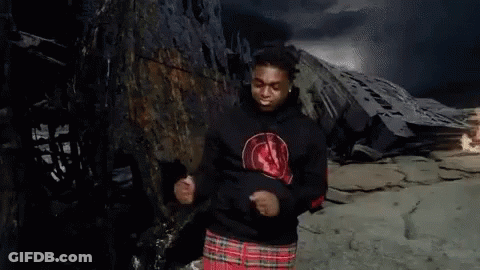 A Man Wearing A Black Hoodie And A Plaid Skirt Is Dancing In Front Of A Mountain . GIF
