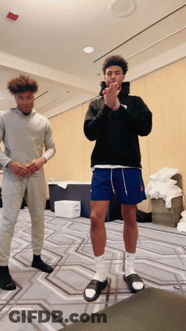 A Man Wearing A Black Hoodie And Blue Shorts Is Standing Next To Another Man GIF