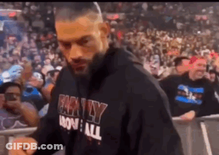 A Man Wearing A Black Hoodie Is Walking In Front Of A Crowd . GIF