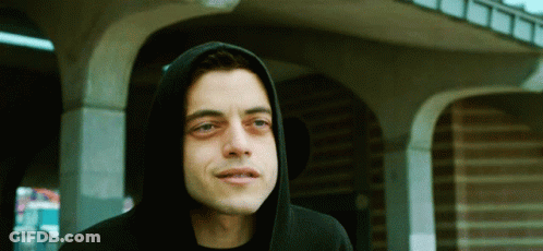A Man Wearing A Black Hoodie Stands In Front Of A Brick Building GIF