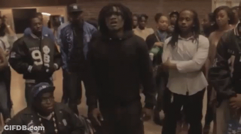A Man Wearing A Black Hoodie With The Number 98 On It Stands In A Crowd Of People GIF