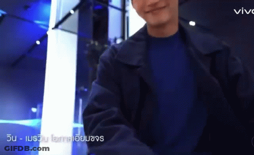 A Man Wearing A Black Jacket And A Blue Shirt Is Standing In A Room . GIF