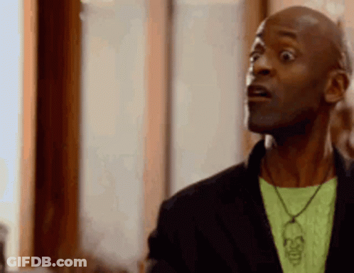 A Man Wearing A Black Jacket And A Green Shirt With A Skull Necklace Is Making A Surprised Face . GIF
