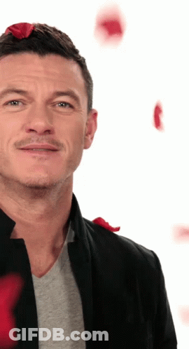 A Man Wearing A Black Jacket And A Grey Shirt With Red Roses On His Head GIF