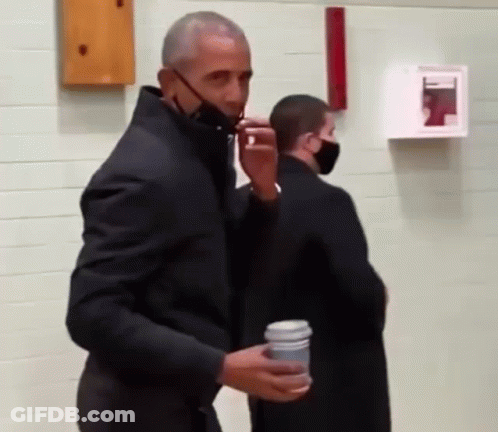 A Man Wearing A Black Jacket And A Mask Is Holding A Cup Of Coffee . GIF