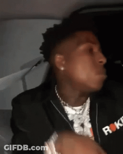 A Man Wearing A Black Jacket And A Necklace Is Sitting In A Car And Making A Funny Face . GIF