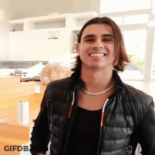 A Man Wearing A Black Jacket And A Necklace Smiles GIF