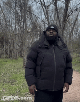 A Man Wearing A Black Jacket And A North Face Hat Is Standing In A Park GIF