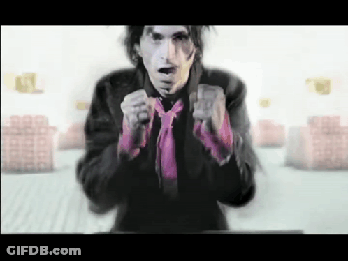 A Man Wearing A Black Jacket And A Pink Tie Is Pointing At The Camera GIF