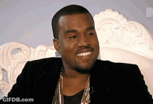 A Man Wearing A Black Jacket And Gold Chains Smiles While Sitting On A White Chair . GIF