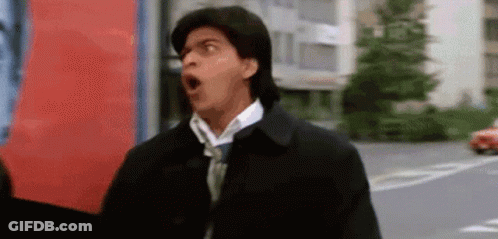 A Man Wearing A Black Jacket And Tie Is Making A Funny Face . GIF
