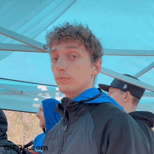 A Man Wearing A Black Jacket With A Blue Hood And A Black Hat With The Letter B On It GIF