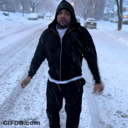 A Man Wearing A Black Jacket With A Hood Is Walking In The Snow GIF