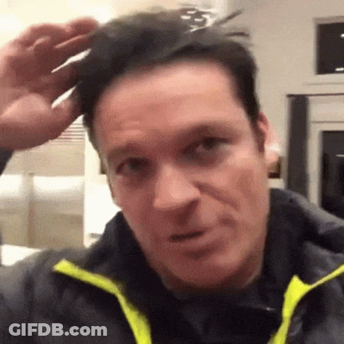 A Man Wearing A Black Jacket With A Yellow Collar Is Holding A Pair Of Scissors To His Head . GIF