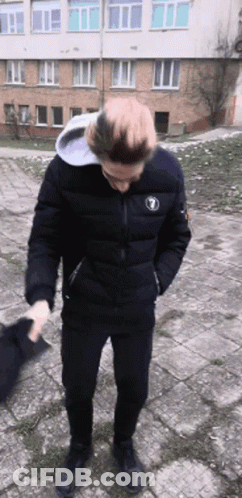A Man Wearing A Black Jacket With The Number 1 On It Is Standing In Front Of A Building GIF