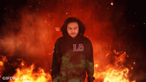 A Man Wearing A Black La Hoodie Stands In Front Of Flames GIF