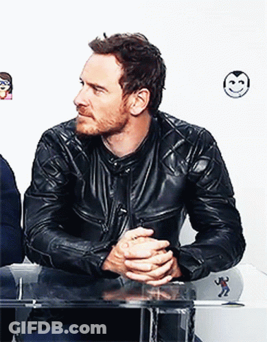 A Man Wearing A Black Leather Jacket Is Sitting At A Table With His Hands Folded GIF