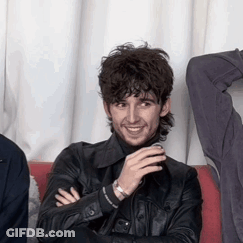 A Man Wearing A Black Leather Jacket Is Smiling With His Arms Crossed GIF
