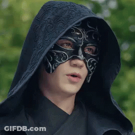 A Man Wearing A Black Mask And A Hood Is Looking At The Camera . GIF