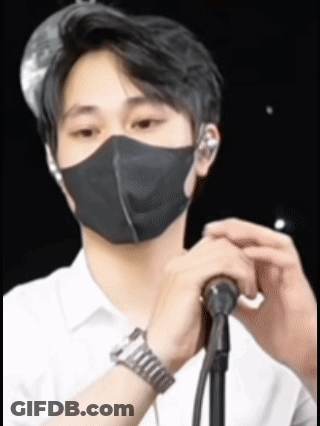 A Man Wearing A Black Mask Is Holding A Microphone In Front Of Him . GIF