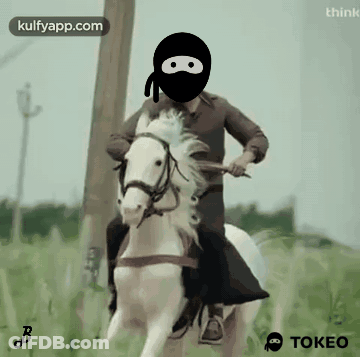 A Man Wearing A Black Mask Is Riding A White Horse In A Field GIF