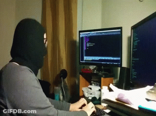 A Man Wearing A Black Mask Is Typing On A Keyboard In Front Of A Computer Monitor GIF