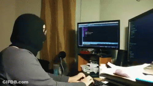 A Man Wearing A Black Mask Is Typing On A Keyboard In Front Of A Computer Monitor . GIF