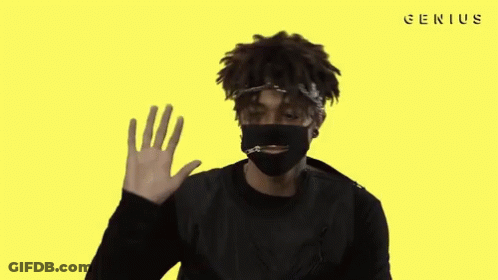 A Man Wearing A Black Mask Is Waving His Hand In Front Of A Yellow Background With The Word Genius On It GIF
