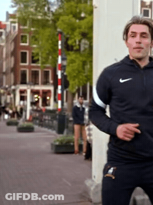 A Man Wearing A Black Nike Jacket Is Standing On A Street GIF