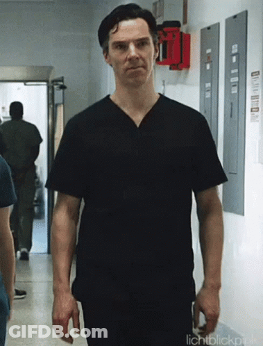 A Man Wearing A Black Scrub Top Is Walking Down A Hallway . GIF