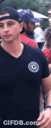 A Man Wearing A Black Shirt And A Baseball Cap Is Standing In A Crowd Of People . GIF