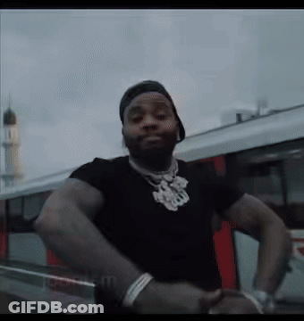 A Man Wearing A Black Shirt And A Hat Is Standing In Front Of A Car . GIF