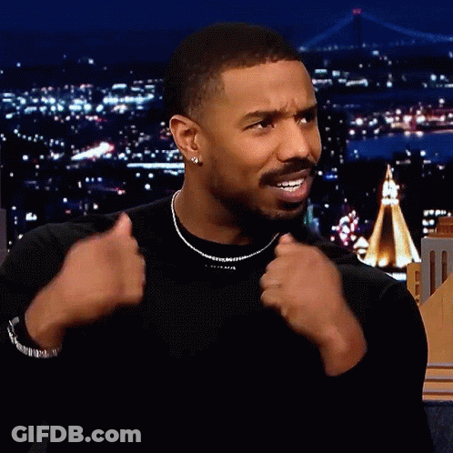 A Man Wearing A Black Shirt And A Necklace Is Giving A Thumbs Up Sign GIF