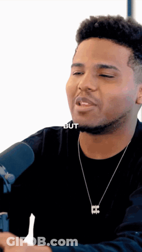 A Man Wearing A Black Shirt And A Necklace With A Letter B On It GIF