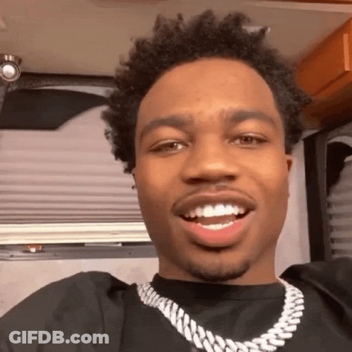 A Man Wearing A Black Shirt And A Silver Chain Is Smiling For The Camera GIF